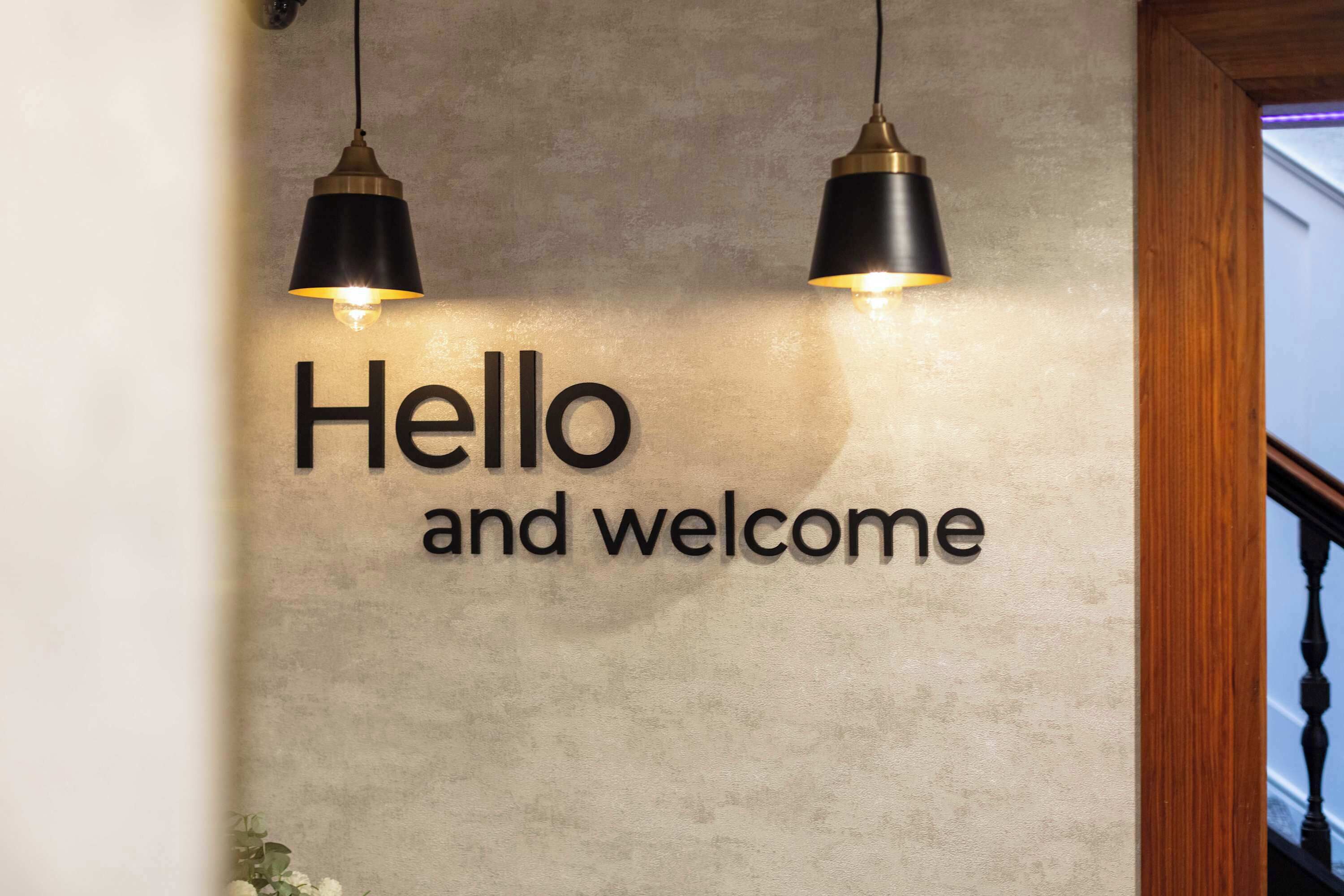 Un muro con il testo 'Hello and welcome' e due lampade a sospensione.