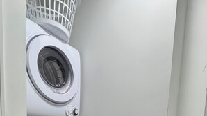 A laundry room with a washing machine and dryer, a white wall, and a wooden floor. - Elegant Studio Near Boston (Malden)