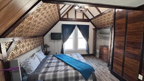 A bedroom with a sloped ceiling, a bed with a blue blanket, a TV, and a wardrobe. - Elegant Studio Near Boston (Malden)