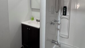 A modern bathroom with a glass-enclosed shower, a white bathtub, a sink with a mirror, and dark-toned cabinets. - Elegant Studio Near Boston (Malden)