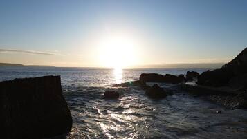 A coastal scene with the sun low on the horizon, reflecting off the water.