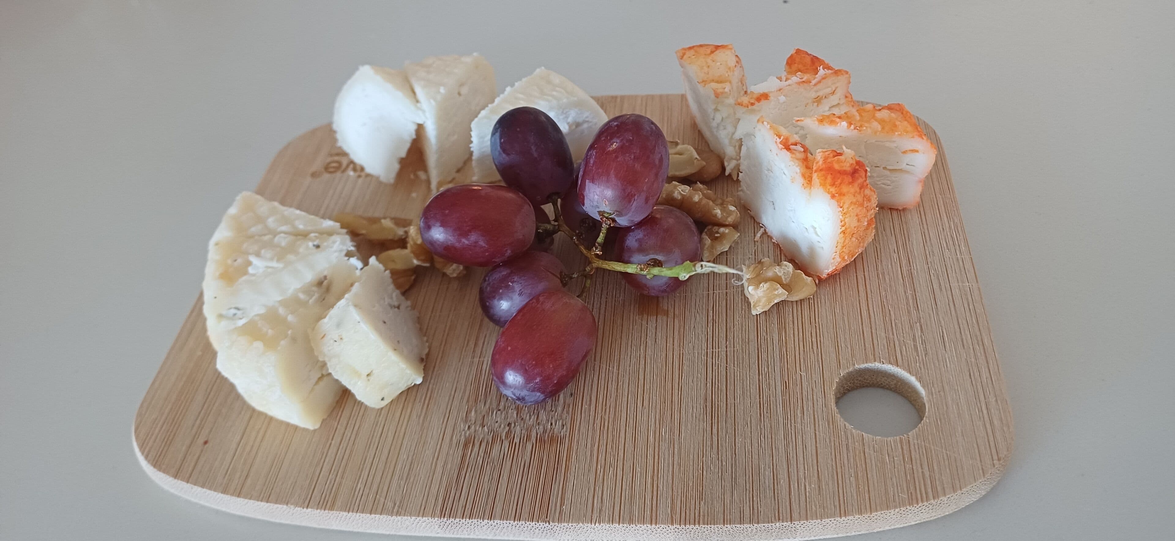 A wooden board with cheese, grapes, and bread.
