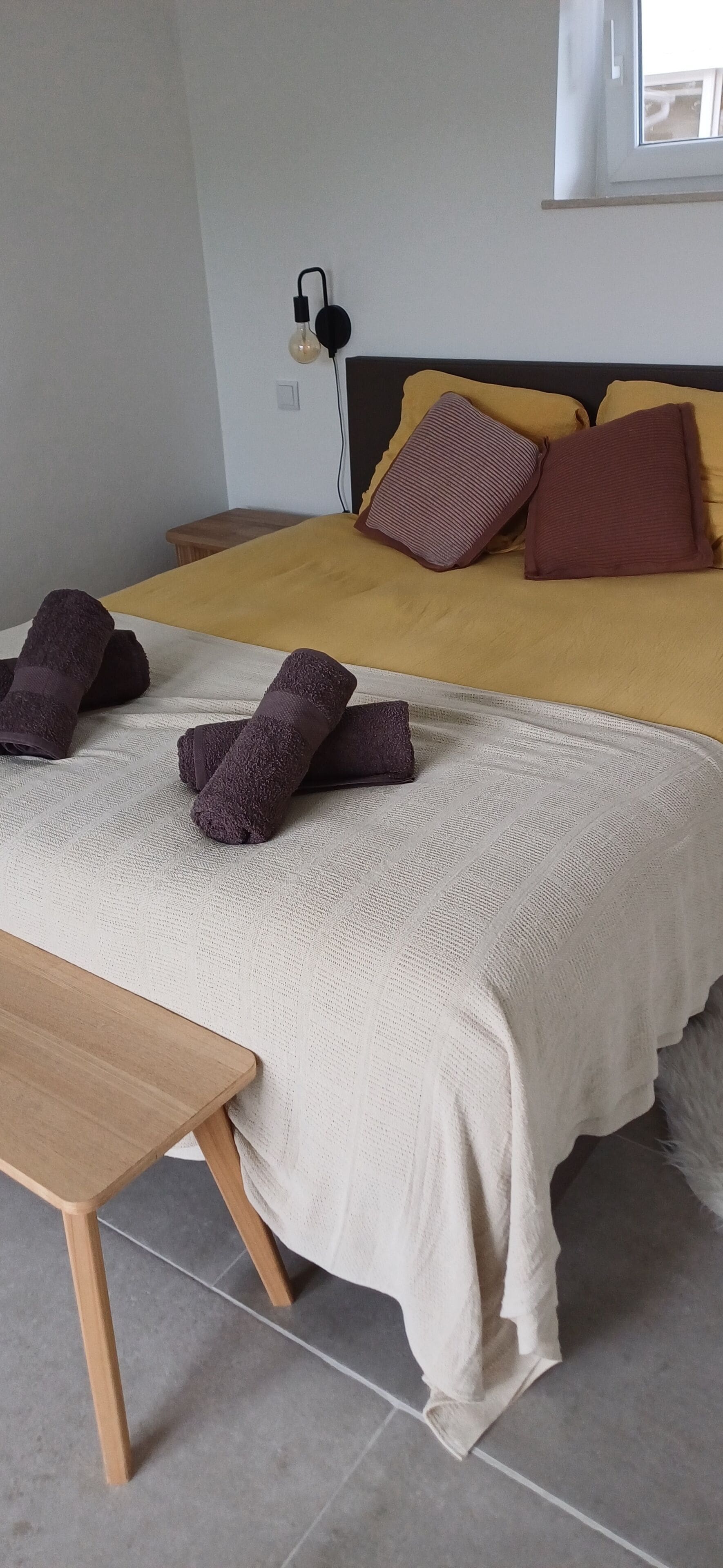 A neatly made bed with a white and yellow bedspread, two brown pillows, and a pair of folded towels on the bed.