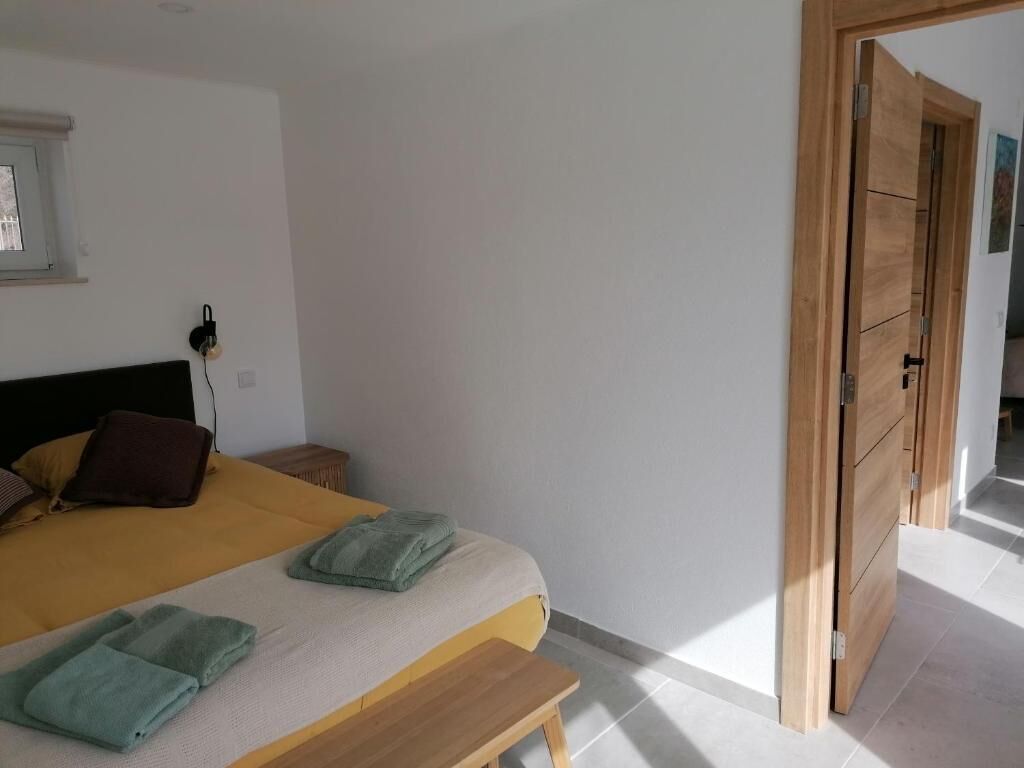 Un dormitorio con cama, almohadas, una mesita de noche, una lámpara de pared y una puerta de madera.