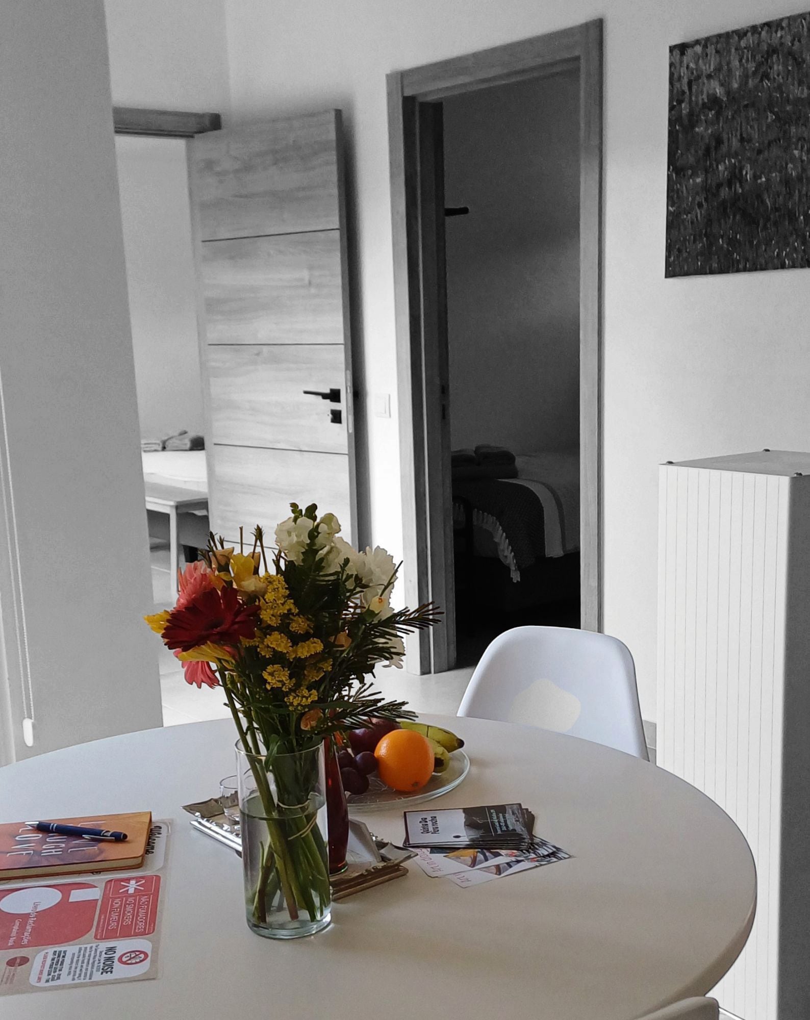 A dining table with a vase of flowers, a plate of fruit, and some papers.