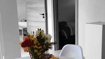 A dining table with a vase of flowers, a plate of fruit, and some papers.