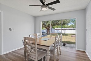 Ein Essbereich mit Holztisch und Stühlen, einem Deckenventilator und einer Glasschiebetür, die zu einem Garten führt.