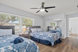 Ein Schlafzimmer mit zwei Betten, einem Deckenventilator und großen Fenstern.