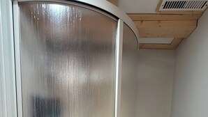 A room with a curved metallic door, a small wooden shelf with towels, a vent on the ceiling, and tiled flooring. - Peaceful Oasis Private Basement Suite With Queen Bed & Full Kitchen (Shawinigan)