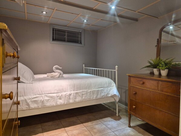 A bedroom with a bed, a dresser, a mirror, a window with blinds, and a ceiling with recessed lighting. - Peaceful Oasis Private Basement Suite With Queen Bed & Full Kitchen (Shawinigan)