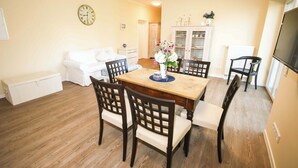 Un coin repas avec une table et des chaises en bois, un canapé blanc, une horloge au mur et un meuble avec des portes en verre.