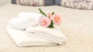 Une pile de serviettes blanches, soigneusement pliées, est posée sur un lit. En arrière-plan, on aperçoit un coussin à motifs floraux.