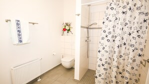 Une salle de bain avec un radiateur blanc, des toilettes, un rideau de douche orné de motifs d’étoiles de mer et une serviette à bordure bleue.
