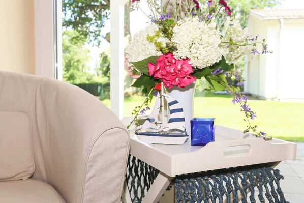 Un canapé beige, une petite table d’appoint blanche avec un vase de fleurs et une bougie bleue.