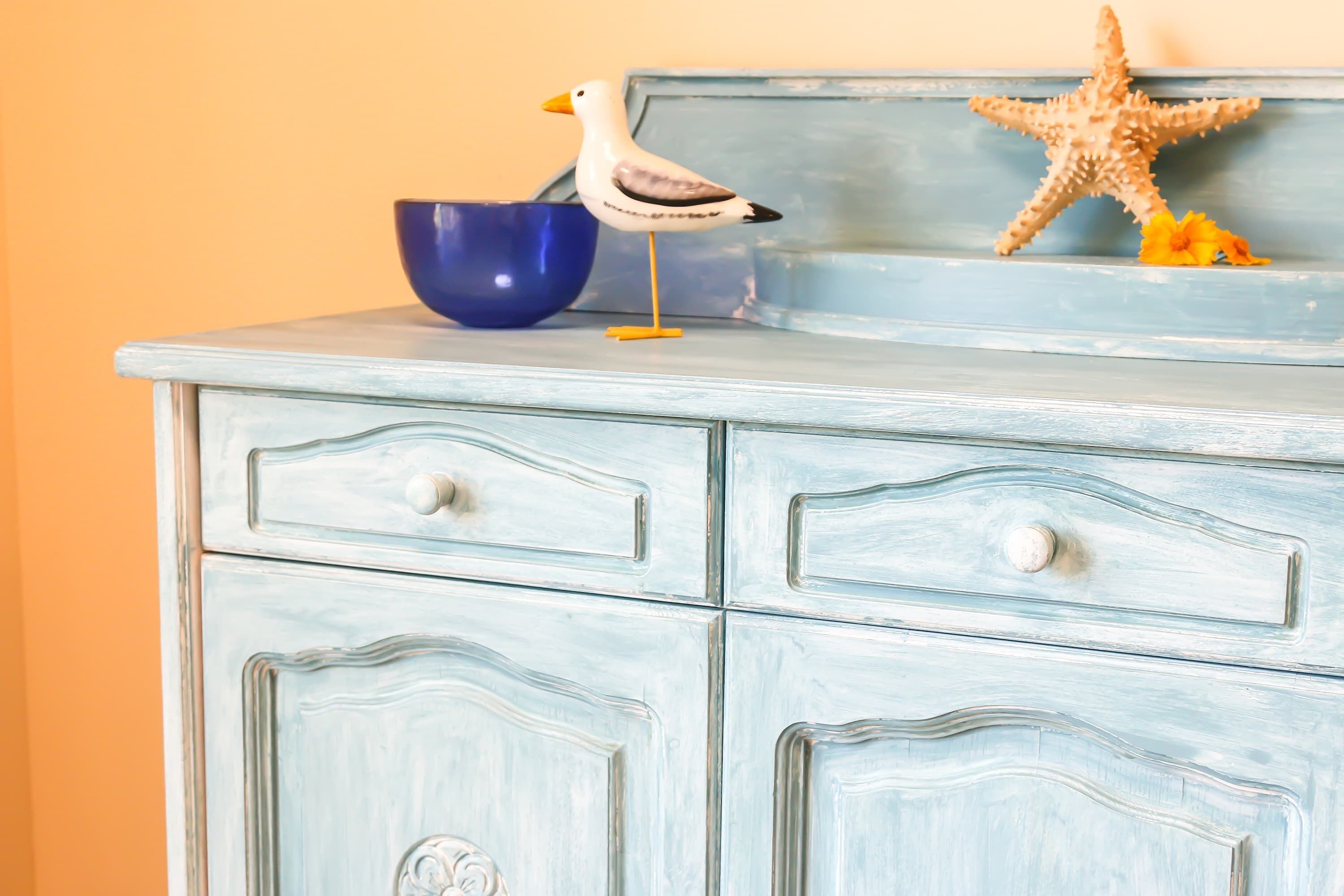 A light blue dresser with two drawers, a blue bowl, a seagull figurine, and a starfish.