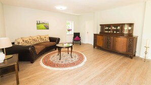 A living room with a sofa, a round coffee table, a cabinet, and a window with a view of a garden. - FeWo Nostalgie im Ferienidyll am Großen Wentowsee (Gransee)
