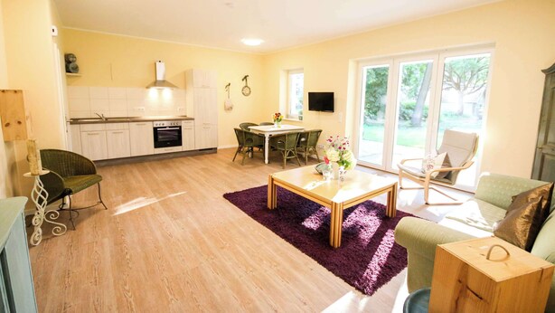A modern living room with a dining area, kitchen, and large windows. - FeWo Cottage im Ferienidyll am Großen Wentowsee (Gransee)