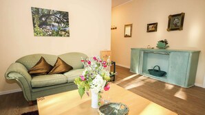 A living room with a green sofa, a wooden coffee table, a vase with flowers, and a teal cabinet with a basket. - FeWo Cottage im Ferienidyll am Großen Wentowsee (Gransee)