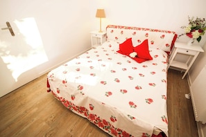 A bedroom with a floral bedspread, a red pillow, a bedside lamp, a nightstand, and a vase with flowers. - FeWo Cottage im Ferienidyll am Großen Wentowsee (Gransee)