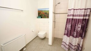 A bathroom with a toilet, shower, radiator, and a painting on the wall. - FeWo Cottage im Ferienidyll am Großen Wentowsee (Gransee)