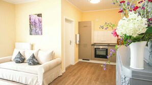 A living room with a sofa, a white vase with flowers, a kitchen in the background, and a door. - FeWo Klassisch – Ihrem Rückzugsort direkt am Großen Wentowsee (Gransee)