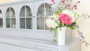A white cabinet with glass doors, a vase with flowers, and a wall outlet. - FeWo Klassisch – Ihrem Rückzugsort direkt am Großen Wentowsee (Gransee)