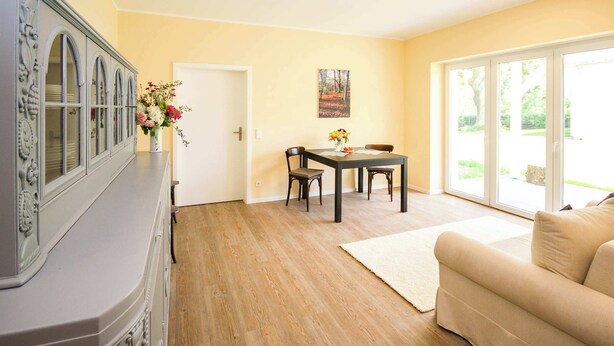 A room with a dining table, chairs, a sofa, a cabinet, and a door leading to a balcony. - FeWo Klassisch – Ihrem Rückzugsort direkt am Großen Wentowsee (Gransee)
