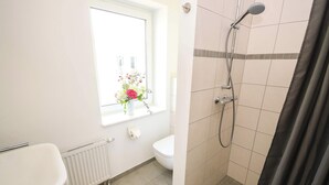 A bathroom with a white sink, toilet, shower, and a window with a flower arrangement. - FeWo Klassisch – Ihrem Rückzugsort direkt am Großen Wentowsee (Gransee)