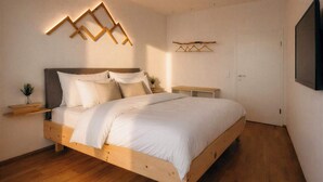 A bedroom with a wooden bed, bedside tables, a wall-mounted TV, and a hanging light fixture. - BERGNEST – Private Terrace & Garden (Voldöpp)