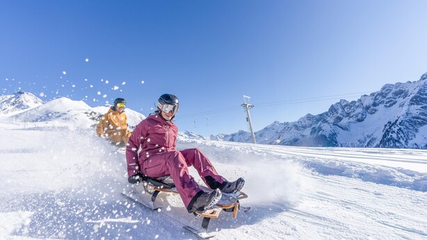 A snow-covered slope with a person in a purple outfit sitting on a sled. - BERGNEST – Private Terrace & Garden (Voldöpp)