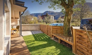 A backyard with a wooden deck, a grassy area, and a view of mountains.