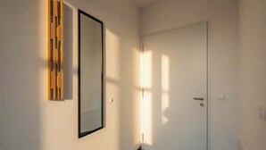 A hallway with a white door, a framed mirror, and a wooden panel on the wall. - BERGNEST – Private Terrace & Garden (Voldöpp)