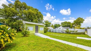 A green house with a door, a small garden, and a white fence. - Miami Tree House Renovated Beach Jacuzzi (Miami)