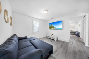 A modern room with a grey sofa, a flat-screen TV, and a white coffee table. - Miami Tree House Renovated Beach Jacuzzi (Miami)