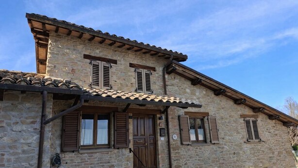 A stone building with a wooden door, shutters, and a tiled roof. - Affittacamere Castelmanardo (Amandola)