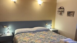 A bedroom with a wooden ceiling, a floral bedspread, two bedside lamps, and a wall-mounted shelf with a picture. - Affittacamere Castelmanardo (Amandola)