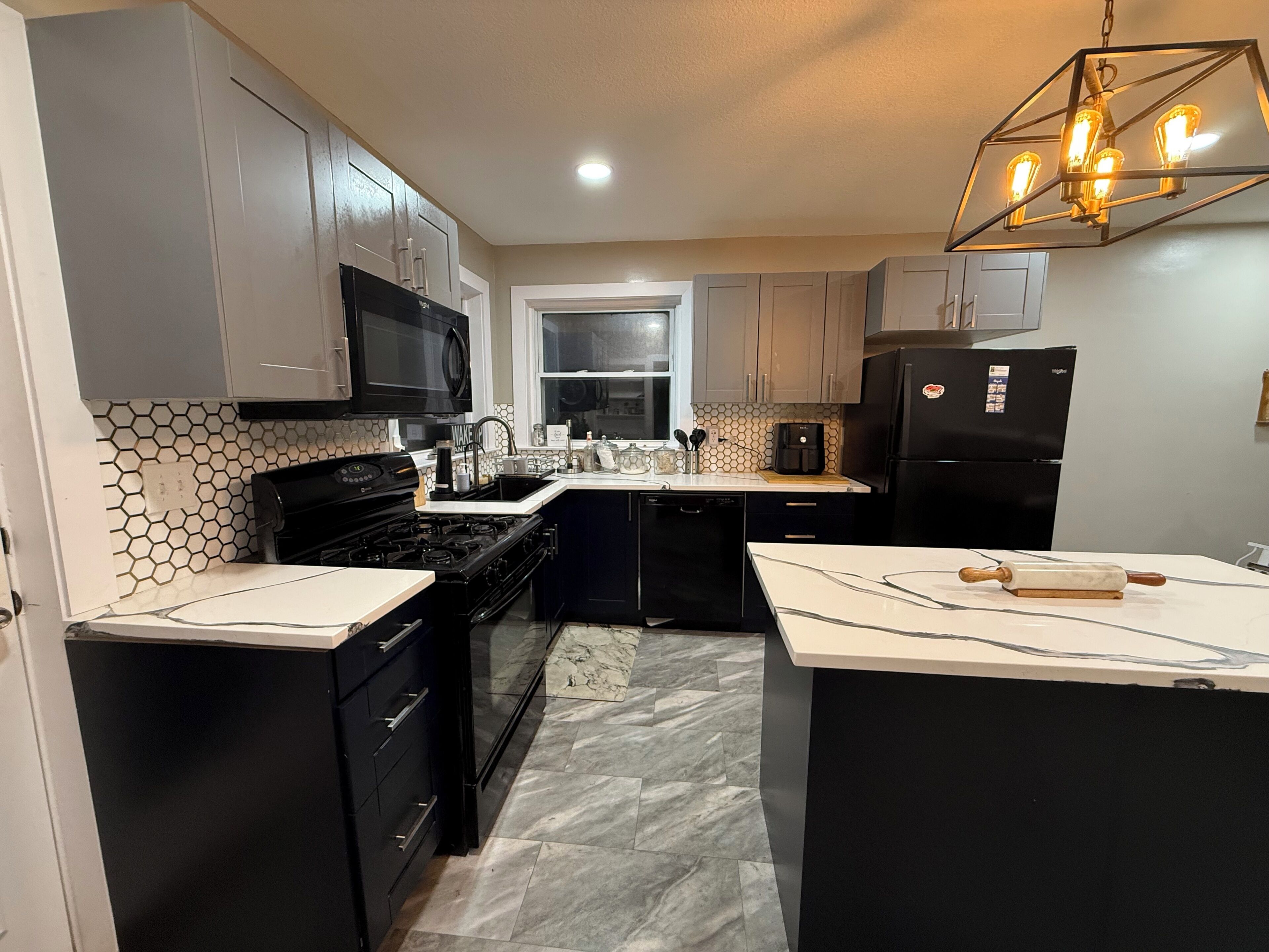 A modern kitchen with a central island, black appliances, and a hexagonal tile backsplash.