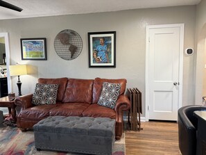 Ein Wohnzimmer mit einem braunen Ledersofa, einem grauen Hocker, einem gerahmten Fußball und einem gerahmten Bild eines Fußballspielers.