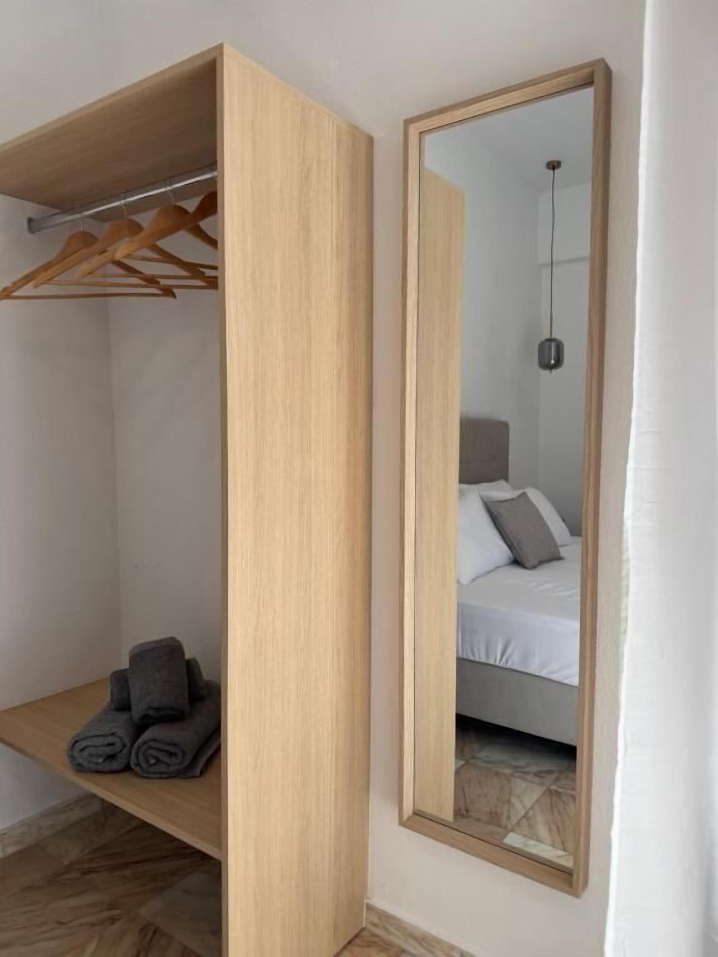 Een kamer met een houten garderobe, een spiegel, een bed met kussens en een hanglamp.