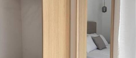 Quarto com guarda-roupa de madeira, espelho, cama com almofadas e luminária suspensa.