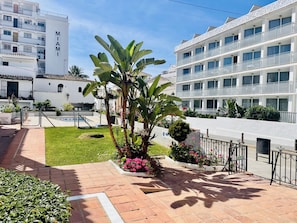 A courtyard with a paved walkway, a small garden with plants and flowers, and a multi-story building with balconies. - Apartamento Azure Burriana by At Home Costa del So (Nerja)