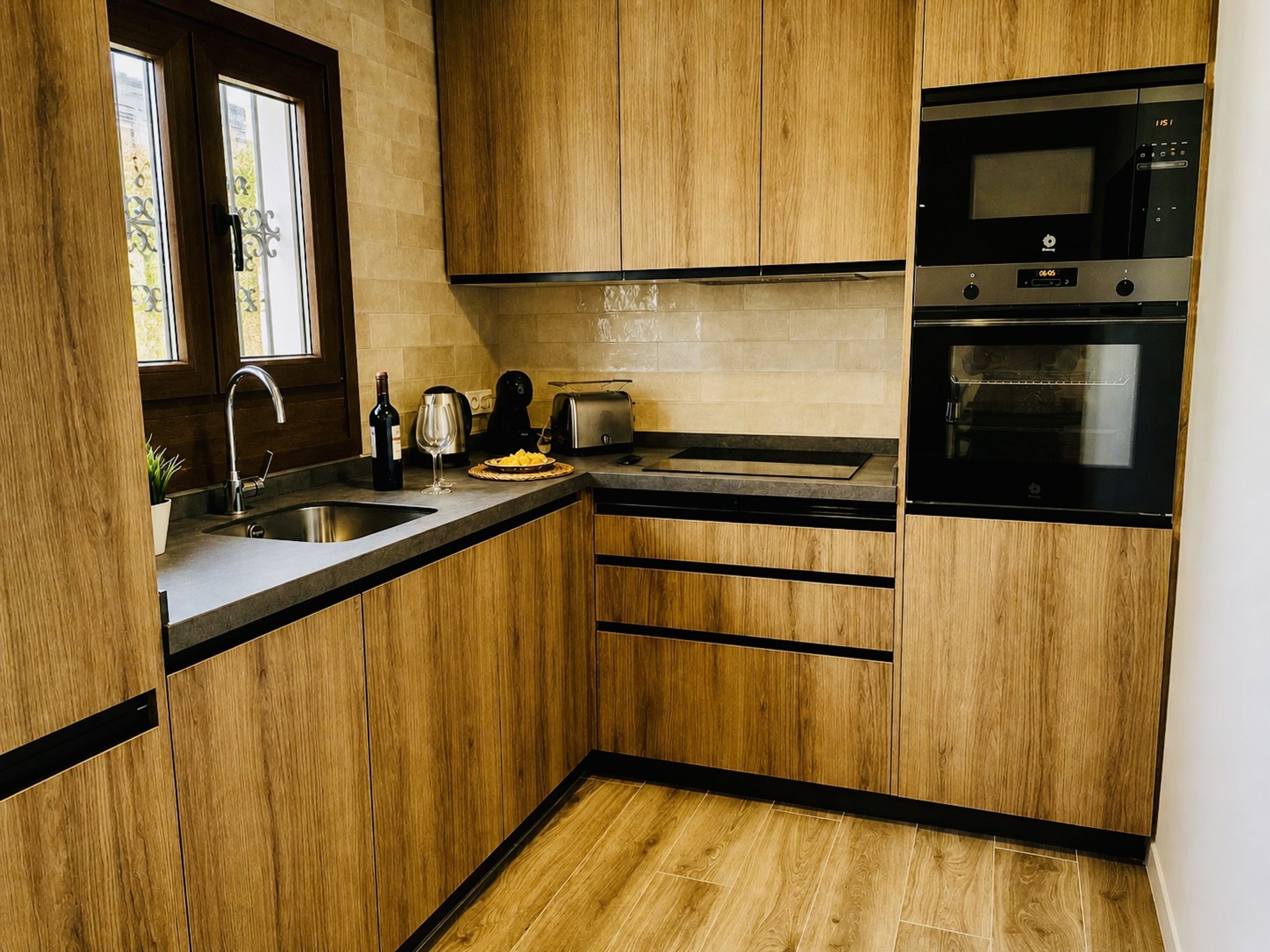 A modern kitchen with wooden cabinets, a stainless steel sink, a toaster, and an oven.