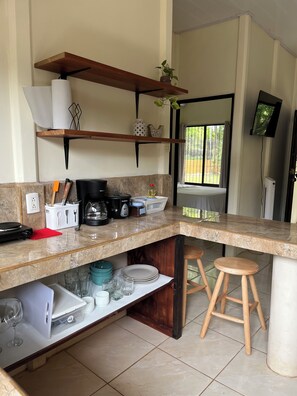 Een keuken met een marmeren aanrecht, houten krukken, een koffieapparaat en een aan de muur bevestigde televisie.