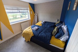 Ein Schlafzimmer mit einem Bett, einem Fenster, einem Heizkörper und einer Wand mit geometrischem Muster.