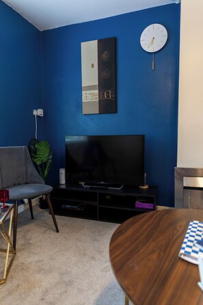 Ein Wohnzimmer mit Fernseher, einer Uhr, einem Sofa und einem Tisch.