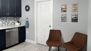 Una cucina con mobili scuri, una porta bianca e decorazioni murali tra cui cartelli con la scritta 'Il caffè è più buono al lago'.
