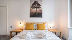 Ein Bett mit gestreifter Bettwäsche, zwei Kissen, zwei Nachttische mit Lampen und ein an der Wand hängendes Bild von einem Baum.