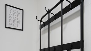 Ein schwarzer Kleiderhaken aus Metall mit Haken, eine schwarze Ablage und ein gerahmtes Schild an der Wand.
