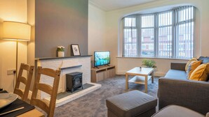 Ein Wohnzimmer mit Kamin, Fernseher, Sofa und einem Fenster mit Jalousien.