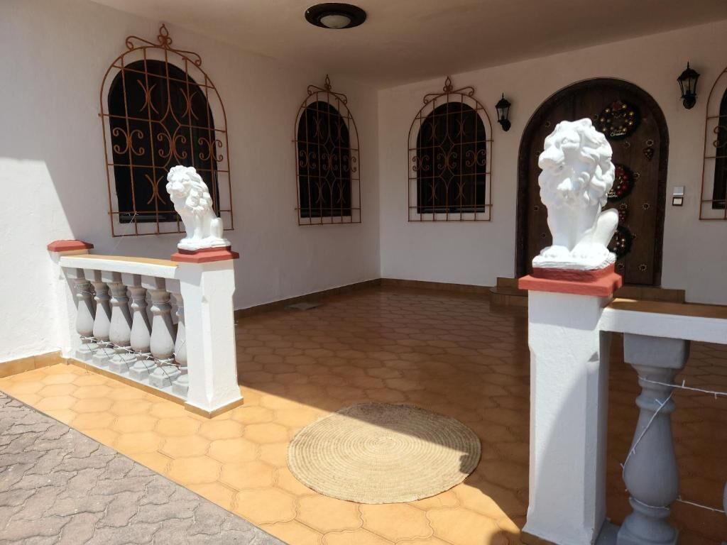 A building entrance with a white balustrade, a woven mat, and three arched windows with decorative metal grilles.
